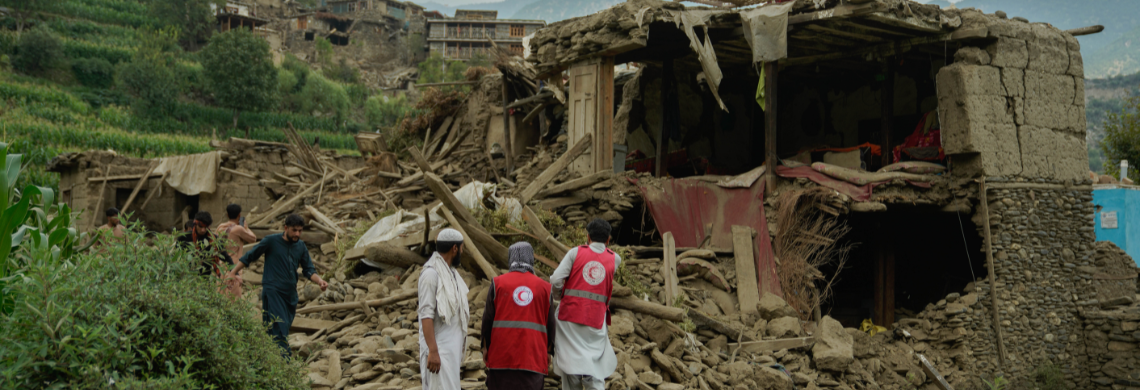 Man sieht ein Bild eines zerstörten Hauses und Helfer des Roten Kreuzes.